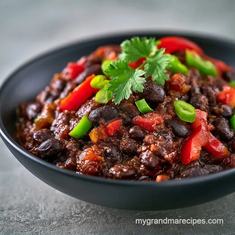 Deep bowl of dark bean stew topped with a swirl of white sour cream, creamy avocado slices, and a fresh lime wedge.